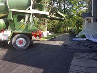 Showing protective measures, cement truck, and special cart for moving cement to form for base of residential basketball court in shades of blue in Lexington, MA.