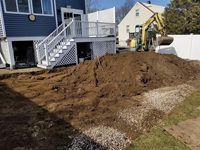 Excavation to prepare the site of a small blue and grey basketball court in Braintree, MA, adjacent to existing pool and featuring a custom H logo.