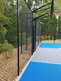 Blue and gray residential basketball court in Easton, MA, viewed from back side, highlighting fence and goal.