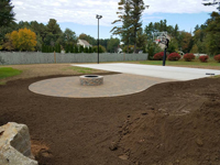 Under construction basketball court featuring Celtics logo, with fire pit, patio, and light for night play, in Londonderry, NH.