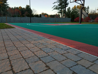 Closeup of periphery and surface of completed basketball court featuring Celtics logo, with fire pit, patio, and light for night play, in Londonderry, NH.