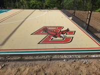 Closeup of custom Boston College Eagles logo on corner of sand and green backyard basketball multicourt in Londonderry, NH.