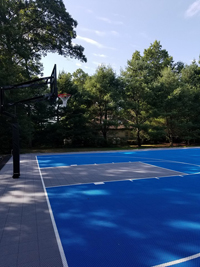 Large royal blue and titanium basketball court with golf seahorse logo at Bay Club in Mattapoisett, MA, shown from side looking at hoop at one end.