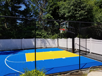 Royal blue and yellow basketball court and accessories in Stoneham, MA, viewed from adjacent covered pool.