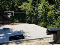 Dry concrete base is ready for installation of low impact tiles for black and grey home backyard basketball court in Wellesley, MA.