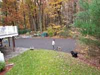 Olive green and grey basketball court with hoop and fencing in Hopkinton, MA. Packing powdered stone as final underlay layer for concrete base.