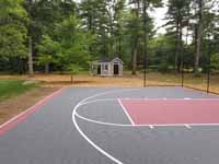 Partial view of Middleboro, MA basketball court from right end, with shed visible in background. Optional fencing included with charcoal and rust court surface.