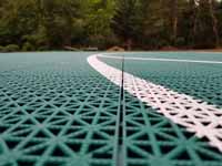 Green and red residential basketball court in Middleborough, MA. Closeup of white line also shows tile detail, designed for comfort and drainage.u