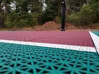 Green and red residential basketball court in Middleborough, MA. This is detail of the tile surface, designed to drain water so there's no puddling.