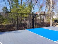 Angled partial view from left highlightin key and hoop area and rebound fence of backyard basketball court in Middleton, MA.