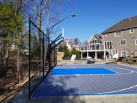View across length of home basketball court from left end, highlighting backing fence and lighting system for night play, in Middleton, MA.