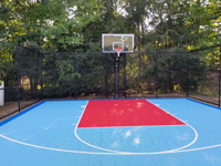 View of basketball court straight toward goal, showing rays of sun on red and blue tile surfaces, in North Attleboro, MA.