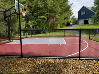 View of kid running to use red and grey home basketball court in Groton, MA.
