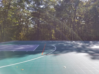 Part of an end zone of large emerald green and titanium backyard basketball court in Bolton, MA, complete with sunbows.