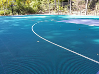 Closer view of tile surface of part of large emerald green and titanium backyard basketball court in Bolton, MA, showing off hoop system and containment fence.
