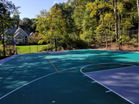 View of about two-thirds of large emerald green and titanium backyard basketball court in Bolton, MA, giving a decent look at the secondary game lines in orange.