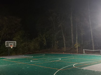 Large emerald green and titanium backyard basketball court in Bolton, MA, lit by energy efficient overhead LED lighting system for night play.