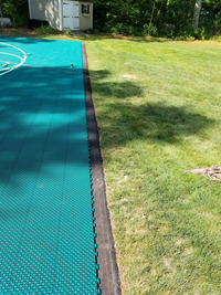 Edge of almost finished emerald green and royal blue basketball court over asphalt in Rehoboth, MA.
