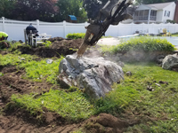Boulder being broken down to make way for a royal blue and yellow basketball court and accessories in Stoneham, MA.