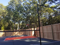 Focus on the hoop, containment fencing, and custom fencing on top of customer's wooden fence for this home basketball court in Walpole, MA.