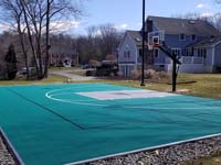 Angled view from back, across surface of residential basketball court toward residence in Reading, MA.